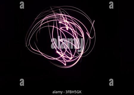 Peinture lumineuse abstraite mettant en scène des lignes roses vibrantes et lumineuses formant des tourbillons et des courbes dynamiques sur un fond complètement sombre en exposition longue Banque D'Images