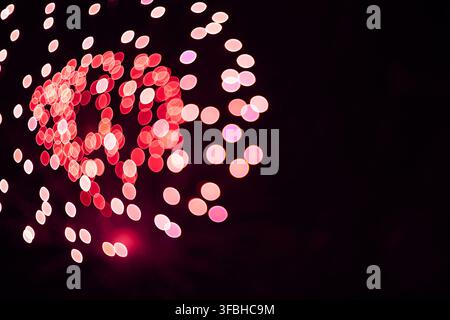 Photographie abstraite à longue exposition de feux d'artifice colorés créant des cercles bokeh rouge et rose lumineux sur un fond de ciel nocturne sombre. Banque D'Images