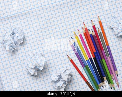 crayons en bois multicolores et feuilles de papier froissés sur fond de papier blanc quadrillé, vue du dessus Banque D'Images