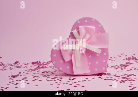 Boîte cadeau rose fermée sous la forme d'un cœur avec un arc sur un fond rose, fond de fête Banque D'Images