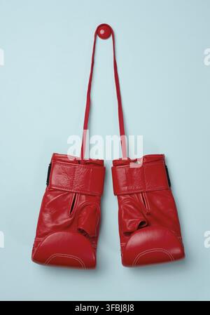 Gants de boxe en cuir rouge suspendus sur un cordon, fond bleu. Équipements sportifs Banque D'Images