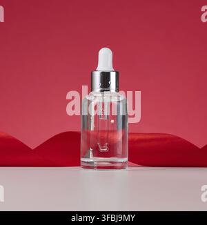 Flacon blanc transparent en verre avec pipette. Contenant pour cosmétiques, acides et huiles sur fond rouge Banque D'Images