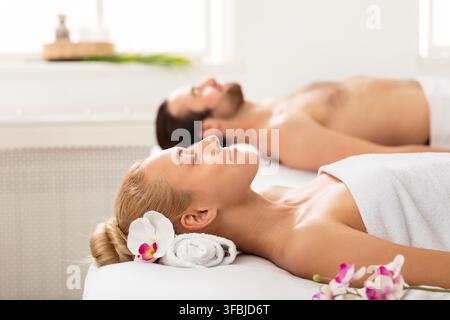Couple détendu allongé enveloppé de serviettes pendant l'aromathérapie détente à l'intérieur Banque D'Images