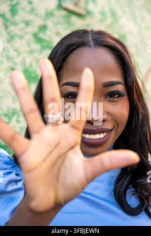 Jeune femme noire souriant, levant la main et interagissant avec le spectateur Banque D'Images