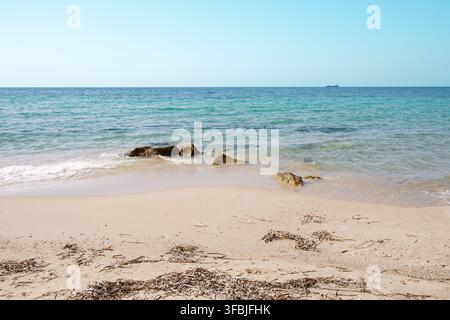 Vue panoramique d'une plage de sable tranquille avec des vagues douces venant s'échouer et une eau de mer turquoise claire rencontrant l'horizon par une journée ensoleillée, en Grèce Banque D'Images