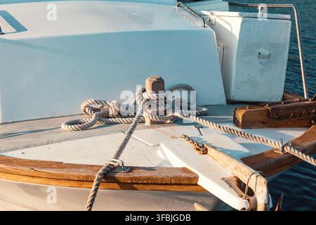 Corde nautique attachée solidement à une bitte en bois sur le pont blanc d'un navire commercial avec de l'eau calme entourant le bateau. Banque D'Images