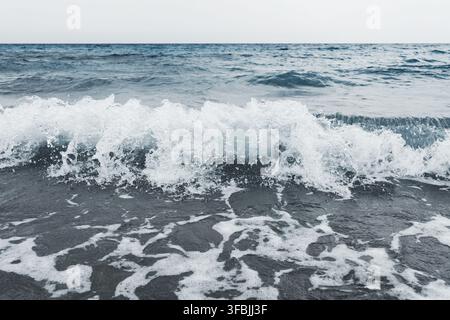 Vague de l'océan s'écrasant sur le rivage sablonneux avec une mousse blanche et des gouttelettes d'eau éclaboussant la surface, Possidi Beach, Grèce. Banque D'Images
