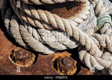 Gros plan de cordages nautiques épais étroitement enroulés autour d'un bittement métallique rouillé et usé avec de grosses boulons rouillés sur un quai de port en Grèce. Banque D'Images