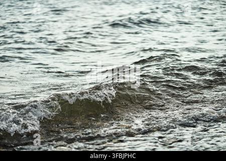 Close up de petites vagues de mer se déplaçant sur une côte rocheuse et éclaboussant des gouttelettes d'eau dans les zones côtières peu profondes pendant la journée, Grèce. Banque D'Images