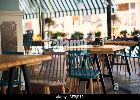 Une terrasse extérieure invitante d'un café avec des tables en bois rustiques et des chaises turquoise vives et grises sous un auvent rayé, Grèce. Banque D'Images