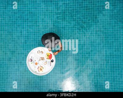 Femme avec chapeau de soleil savourant un plateau de petit-déjeuner flottant Banque D'Images