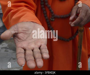 Un sadhou en robes orange traditionnelles tend sa main ouverte pour demander des aumônes, Patan, Népal. Banque D'Images