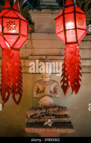 Vue d'une statue de Bouddha en pierre sereine en position de prière, encadrée par deux lanternes en papier traditionnelles rouges lumineuses dans un cadre de temple, Chiang Mai, Thaïlande Banque D'Images
