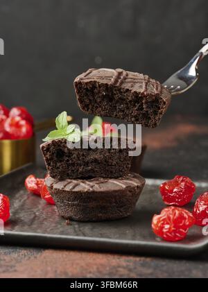 Une pile de riches brownies au chocolat surmontée d'une cerise brillante et d'une feuille de menthe fraîche, debout sur un fond sombre Banque D'Images