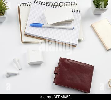 carnets, stylo, pile de cartes de visite, portefeuille en cuir marron et banque d'alimentation avec cordon sur une table blanche, lieu de travail, vue de dessus Banque D'Images