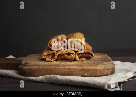 crêpes fines torsadées avec remplissage se trouvent dans une pile sur un panneau en bois, fond noir Banque D'Images