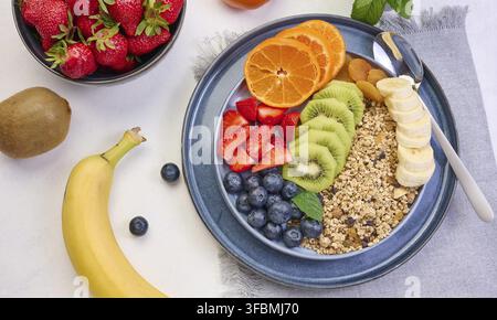 Granola avec fraises, kiwi, banane et bleuets dans une assiette ronde sur une table blanche. Nourriture saine et délicieuse Banque D'Images