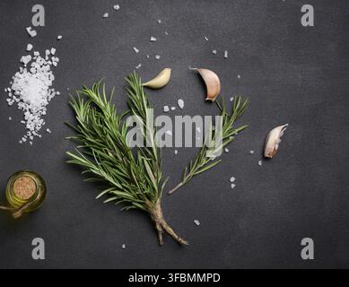 Parsemé de gros sel blanc, de grains de poivre et de brins de romarin sur une table noire, ingrédients pour la cuisson du poisson et de la viande Banque D'Images