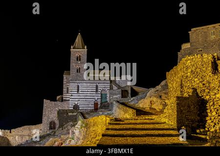 Vue de l'église historique Saint-Pierre à Portovenere illuminée la nuit, présentant sa façade en pierre rayée noire et blanche distinctive et ancie Banque D'Images