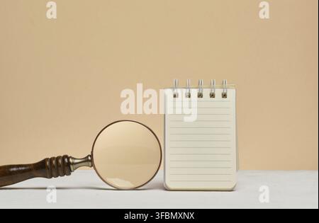 Un cahier ouvert avec des feuilles lignées vierges et une loupe à côté. Recherche d'informations, planification, analyse ou étude Banque D'Images