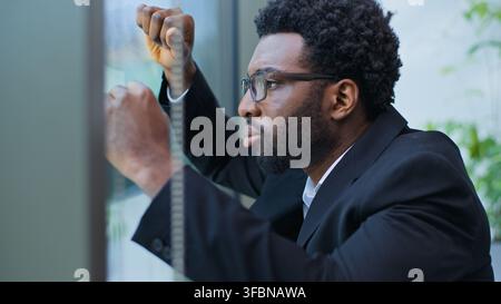 Gros plan d'un homme d'affaires afro-américain inquiet, agacé, stressé, appuyé contre un mur de fenêtre, souffrant de chagrin, homme d'affaires surmené qui souffre Banque D'Images