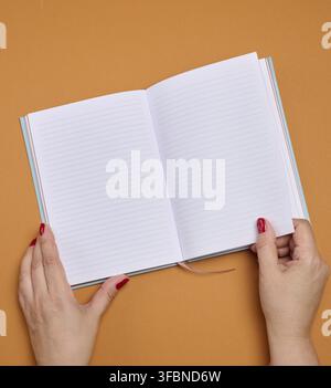 Mains féminines tenant un cahier ouvert avec des pages propres et lignées sur un fond orange. Copier l'espace Banque D'Images