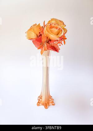 Vase en verre élégante avec des roses artificielles orange et jaunes, isolée sur fond blanc. Banque D'Images