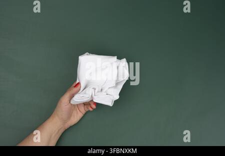 la main d'une femme tient un chiffon blanc sur le fond d'un tableau de craie vert, un endroit pour une inscription Banque D'Images