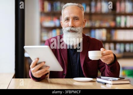 Un homme d'affaires riche et expérimenté boit du café et utilise une tablette numérique Banque D'Images