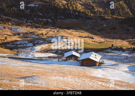 Cabanes traditionnelles de montagne sur des alpages enneigés sous le Seceda dans les Dolomites. Paysage pittoresque avec des chutes de neige fraîche et des couleurs dorées d'automne Banque D'Images
