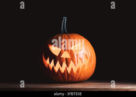 Lanterne de citrouille sculptée effrayante avec lumière de bougie placée sur une surface en bois rustique. Symbole classique d'Halloween brillant dans l'obscurité avec une illumination orange chaude Banque D'Images