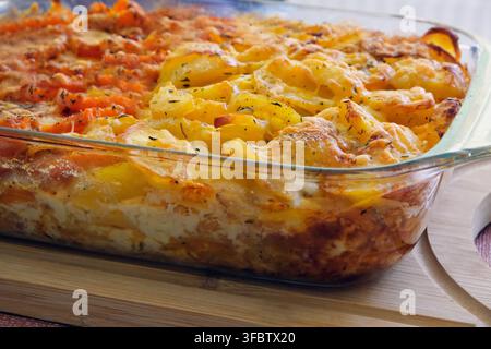 Casserole de gratin de pommes de terre maison avec une croûte de fromage fondu dorée dans un plat de cuisson en verre, servi sur une planche en bois. Banque D'Images