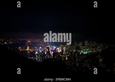 Un panorama aérien capture l’horizon nocturne vibrant de Hong Kong depuis le Pic Victoria, mettant en valeur le port Victoria entouré de nombreuses lumières Banque D'Images