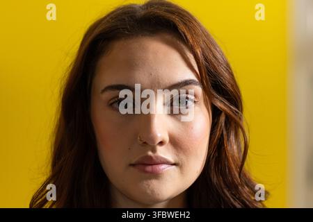 Femme adulte posant en studio devant un fond jaune, montrant un petit anneau de nez et des cheveux ondulés Banque D'Images