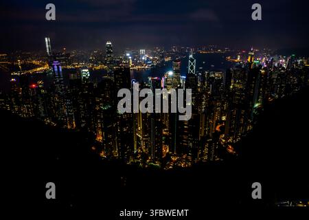 Une vue aérienne nocturne étendue depuis le pic Victoria met en valeur l’éclatant paysage urbain illuminé de Hong Kong, avec ses gratte-ciel densément regroupés Banque D'Images
