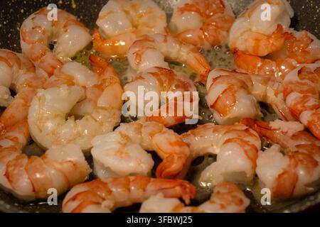 Une poêle remplie d'une fournée de grosses crevettes pelées qui cuisent et grésillent dans le beurre. Banque D'Images
