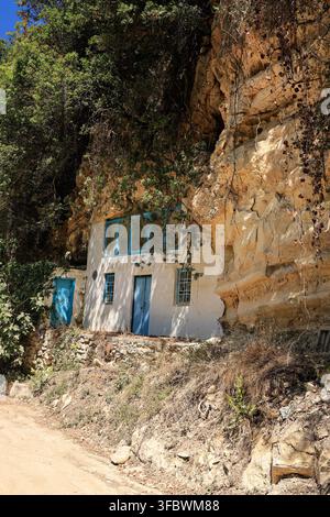 Maison traditionnelle blanchée à la chaux avec des portes bleues intégrée dans une falaise rocheuse, Grèce. Banque D'Images