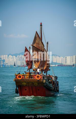 Un bateau junk traditionnel à voile rouge Aqua Luna, peint en rouge et en bois sombre avec des gilets de sauvetage et des pneus orange, croise sur le bleu profond de Victoria H Banque D'Images