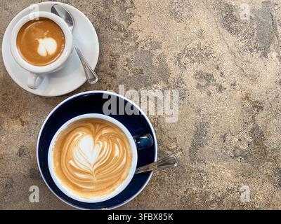 Vue en plan horizontal de deux tasses de café fraîches avec latte art placées sur le côté d'une table en pierre texturée avec espace de copie. Banque D'Images