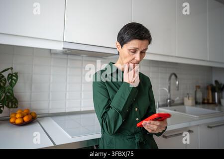 Femme âgée triste et pensive lisant un contenu médiatique perturbant sur son téléphone, nouvelles choquantes causant de la détresse Banque D'Images