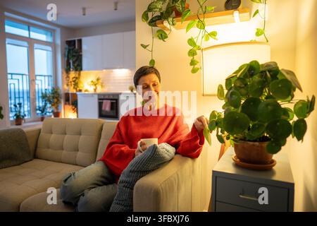 Positive femme senior détendue aime la vie lente et soirée confortable à la maison tout en se reposant sur le canapé. Banque D'Images