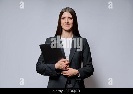 femme d'affaires souriante tenant un ordinateur portable isolée sur fond gris de studio Banque D'Images