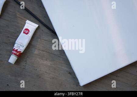 Toile blanche tendue reposant en diagonale sur un établi en bois, avec tube d'huile et corde noire Banque D'Images