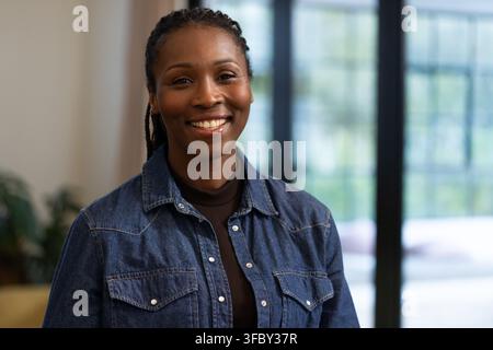 Femme africaine souriant et posant dans le salon, portant une chemise en jean, un col roulé sombre avec porte à grille Banque D'Images