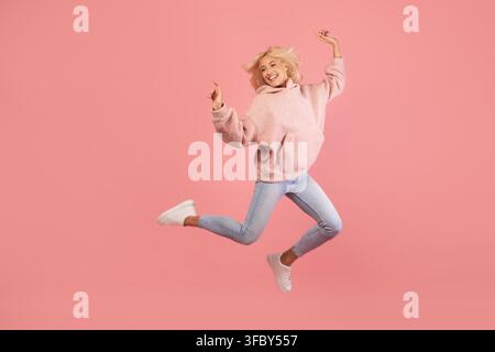Jeune femme joyeuse sautant de joie devant un fond rose, concept de fitness et de style de vie Banque D'Images