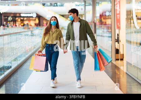 Jeun couple multiculturel heureux faisant ses courses ensemble dans un centre commercial moderne, tenant des sacs de courses colorés Banque D'Images