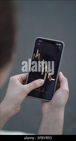 Femme vérifie le graphique Bitcoin sur l'écran du téléphone, se concentrant sur les tendances en chandeliers, les niveaux de prix et les mouvements du marché en tant que trader dévouée. Banque D'Images