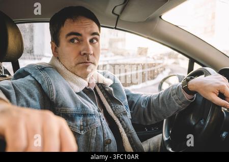 Un homme regarde de derrière le volant de la voiture à l'arrière de la voiture avec étonnement. vue latérale. Banque D'Images