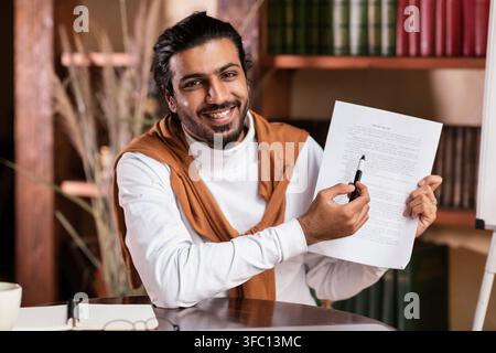 Un bon homme enseignant indien qui montre Essay à l'appareil photo assis à l'intérieur Banque D'Images