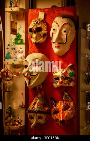 Des masques colorés faits à la main, des visages en céramique peints et des bracelets de perles exposés sur une planche de stand de marché rouge dans une boutique de souvenirs étroite. Banque D'Images